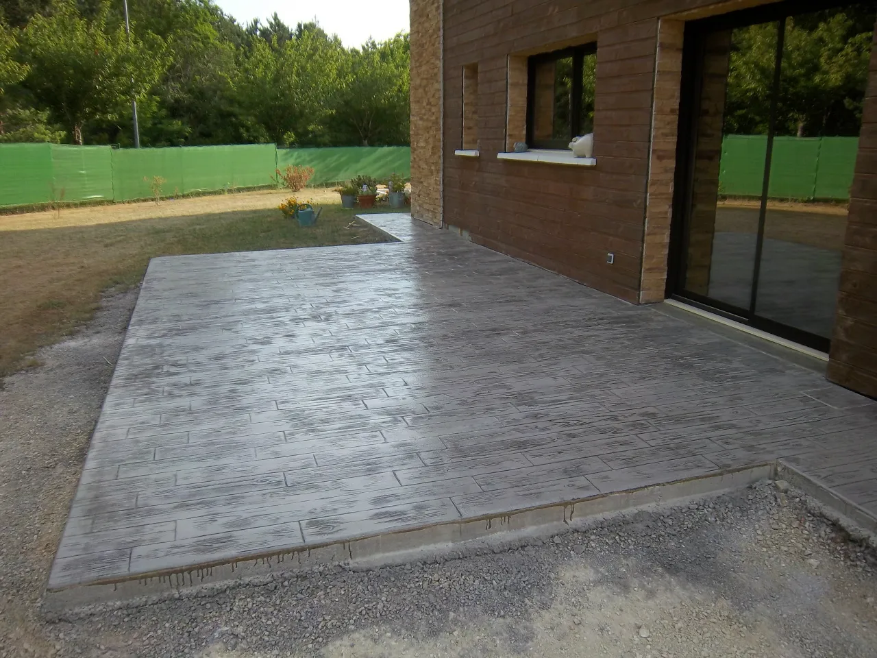 Terrasse en béton imprimé effet lames de bois devant une baie vitrée